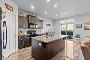 Kitchen with dark brown cabinets, decorative backsplash, recessed lighting, an island with sink, and black appliances
