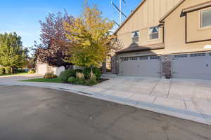 View of front facade with board and batten siding, a garage, concrete driveway, stone siding, and stucco siding