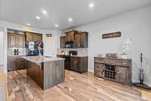 Kitchen with a kitchen breakfast bar, dark brown cabinets, tasteful backsplash, black appliances, and an island with sink