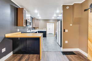 Kitchen featuring a barn door, a peninsula, wooden counters, freestanding refrigerator, and stainless steel microwave
