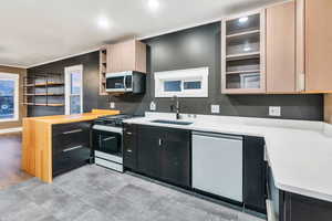 Kitchen featuring stainless steel appliances, glass insert cabinets, dark cabinetry, open shelves, and a peninsula