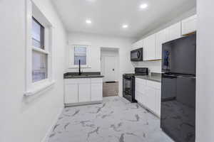 Kitchen with black appliances, white cabinetry, light marble finish floors, recessed lighting, and dark countertops