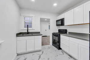 Kitchen with black appliances, white cabinets, light marble finish floors, and recessed lighting