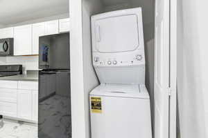 Washroom featuring light marble finish floors and stacked washer / drying machine