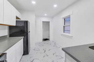 Kitchen with freestanding refrigerator, white cabinets, light marble finish floors, recessed lighting, and dark stone countertops