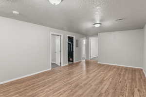 Unfurnished room featuring light wood-type flooring, a textured ceiling, and electric panel