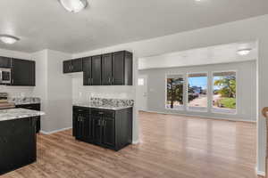 Kitchen featuring dark cabinetry, light wood-type flooring, a textured ceiling, stainless steel appliances, and light stone counters
