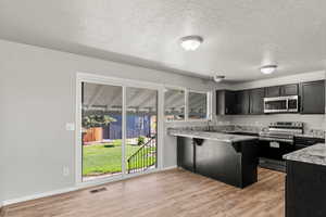 Kitchen featuring appliances with stainless steel finishes, a kitchen breakfast bar, light wood finished floors, a textured ceiling, and a peninsula