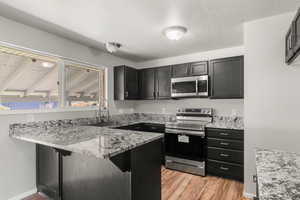 Kitchen with stainless steel appliances, light stone countertops, light wood finished floors, a peninsula, and a textured ceiling