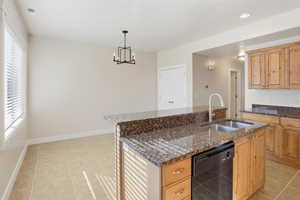 Kitchen featuring light tile patterned floors, dark stone counters, dishwasher, hanging light fixtures, and an island with sink