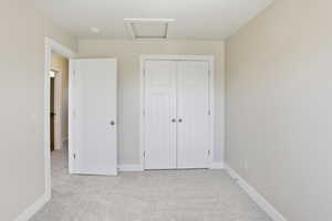 Unfurnished bedroom with carpet floors, attic access, and a closet