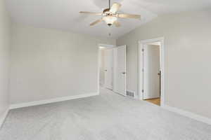 Unfurnished bedroom featuring light carpet, vaulted ceiling, and a ceiling fan