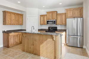 Kitchen with stainless steel appliances, a breakfast bar, dark stone countertops, recessed lighting, and a kitchen island with sink