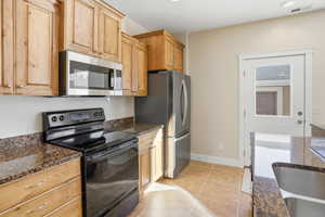 Kitchen with stainless steel appliances, dark stone countertops, light tile patterned floors, light brown cabinetry, and recessed lighting