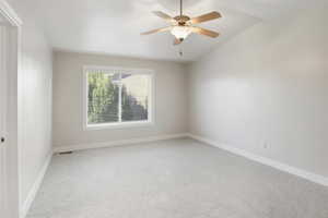 Spare room featuring light colored carpet, vaulted ceiling, and a ceiling fan