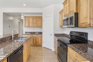 Kitchen featuring black appliances, dark stone counters, light tile patterned flooring, and recessed lighting