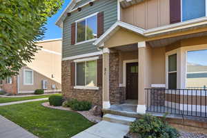 View of exterior entry with stone siding, a yard, covered porch, and board and batten siding