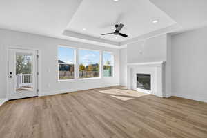 Unfurnished living room with a tray ceiling, recessed lighting, light wood finished floors, a ceiling fan, and a brick fireplace