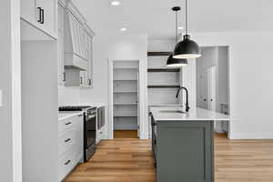 Kitchen with tasteful backsplash, stainless steel range with gas stovetop, a center island with sink, decorative light fixtures, and custom exhaust hood