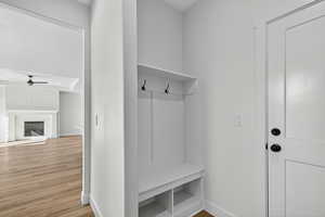 Mudroom featuring a ceiling fan, light wood-type flooring, and a glass covered fireplace