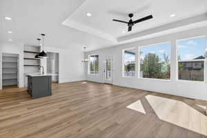 Unfurnished living room with recessed lighting, light wood-style flooring, ceiling fan, a chandelier, and a raised ceiling