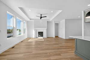 Unfurnished living room featuring a raised ceiling, recessed lighting, a glass covered fireplace, ceiling fan, and light wood finished floors