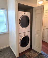 Washroom with stacked washer / dryer and dark wood-type flooring