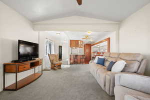 Living area featuring a ceiling fan, light carpet, vaulted ceiling, and healthy amount of natural light