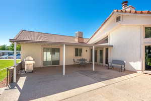 Rear view of property featuring a chimney, stucco siding, a patio, a tile roof, and outdoor dining space