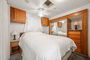 Bedroom with dark colored carpet, ceiling fan, and a closet