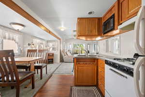 Kitchen with brown cabinets, open floor plan, a peninsula, white appliances, and dark wood-type flooring
