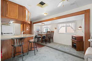 Kitchen with brown cabinets, a breakfast bar area, light countertops, carpet flooring, and glass insert cabinets