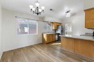 Kitchen with light countertops, pendant lighting, brown cabinetry, a chandelier, and a peninsula