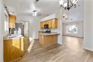 Kitchen featuring ceiling fan, appliances with stainless steel finishes, a chandelier, a peninsula, and light wood finished floors
