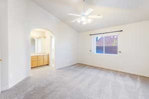 Unfurnished bedroom featuring lofted ceiling, light colored carpet, ceiling fan, ensuite bath, and arched walkways