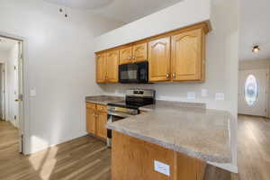 Kitchen with electric stove, light wood-style floors, black microwave, and a peninsula