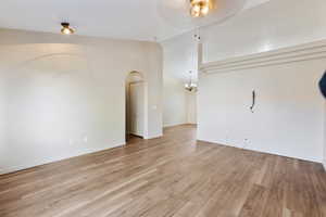 Unfurnished living room with arched walkways, ceiling fan, light wood-style flooring, vaulted ceiling, and a chandelier