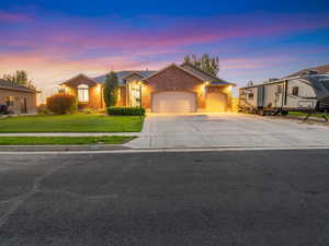 Single story home featuring an attached garage, driveway, a lawn, and brick siding