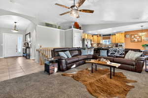 Living area with light tile patterned flooring, a chandelier, a ceiling fan, vaulted ceiling, and light carpet