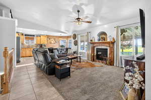 Living room with vaulted ceiling, light tile patterned flooring, a tile fireplace, light carpet, and a ceiling fan