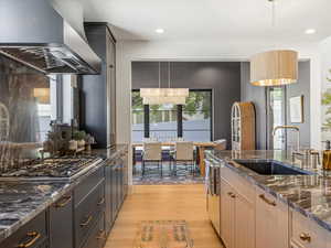 Kitchen with dark stone countertops, wall chimney exhaust hood, decorative light fixtures, and recessed lighting