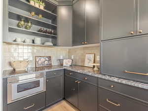 Kitchen featuring open shelves, light stone countertops, backsplash, and gray cabinets