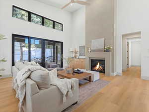Living area with a high ceiling, a glass covered fireplace, light wood-style floors, a ceiling fan, and recessed lighting
