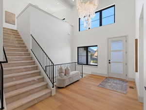 Entryway featuring light wood finished floors, stairway, a chandelier, a high ceiling, and beam ceiling