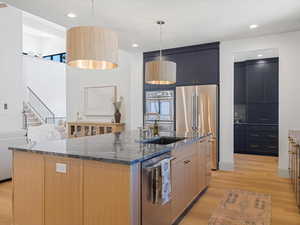 Kitchen with dark stone countertops, light wood-style floors, stainless steel appliances, decorative light fixtures, and recessed lighting