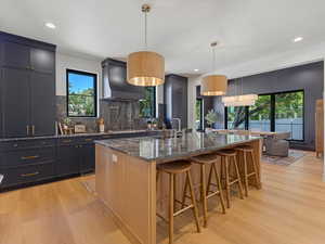 Kitchen featuring dark stone counters, light wood-style flooring, a breakfast bar, pendant lighting, and wall chimney exhaust hood