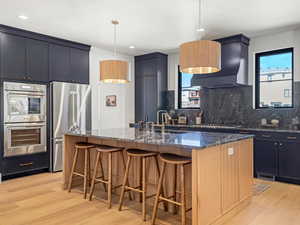 Kitchen with stainless steel appliances, a large island, a kitchen bar, dark stone counters, and light wood finished floors