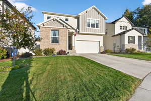 Craftsman house featuring board and batten siding, driveway, an attached garage, a front yard, and brick siding