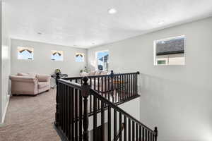 Hall with an upstairs landing, plenty of natural light, a textured ceiling, carpet flooring, and recessed lighting