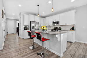 Kitchen featuring a kitchen breakfast bar, tasteful backsplash, white cabinets, light stone counters, and a kitchen island with sink